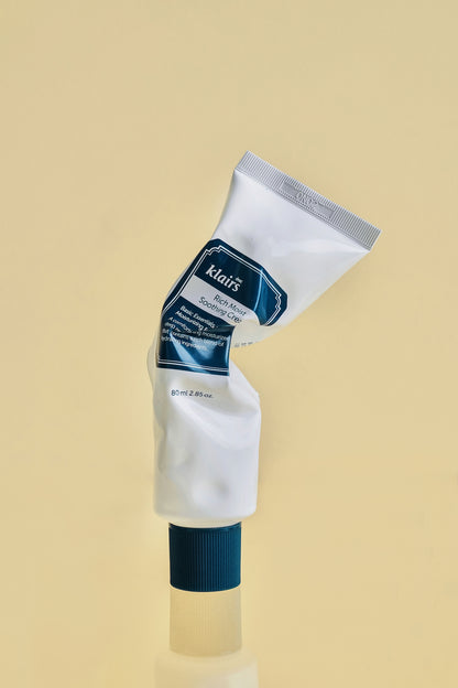 Upright bottle of Klairs Rich Moist Soothing Cream that has been squeezed and is misformed, against a light yellow background.