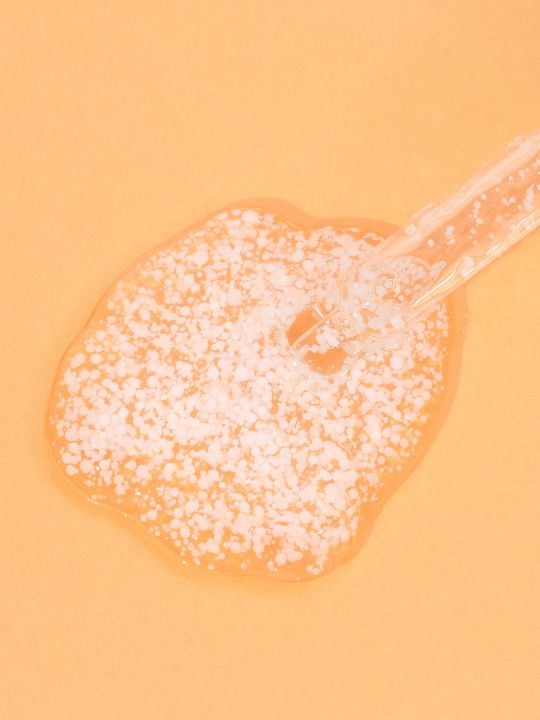 Meisani Glow Drops Vitamin C Serum dropper with close up texture on a orange background