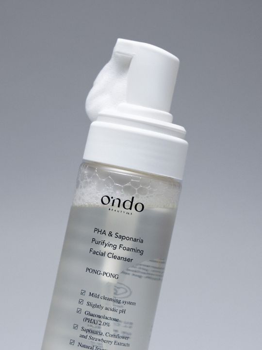 Close up of Ondo Beauty 36.5 PHA & Saponaria Purifying Foaming Cleanser pump with foam coming out, against a grey background