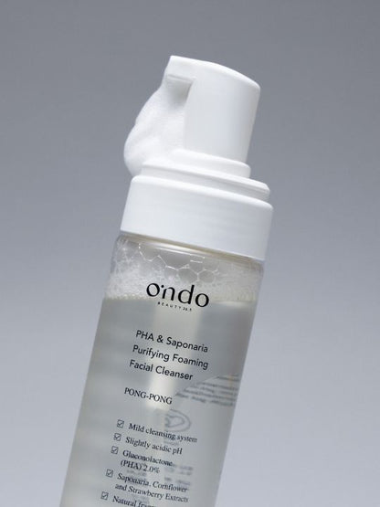 Close up of Ondo Beauty 36.5 PHA & Saponaria Purifying Foaming Cleanser pump with foam coming out, against a grey background