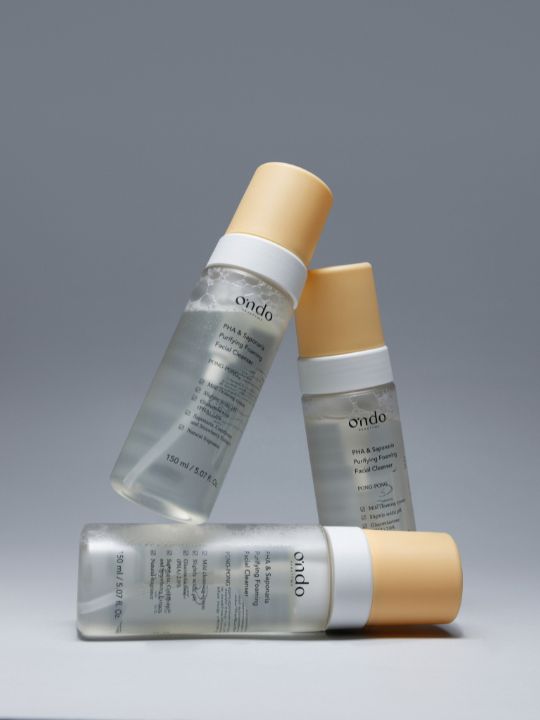 Three bottles of Ondo Beauty 36.5 PHA & Saponaria Purifying Foaming Cleanser arranged in a triangle against a light grey background