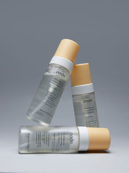 Three bottles of Ondo Beauty 36.5 PHA & Saponaria Purifying Foaming Cleanser arranged in a triangle against a light grey background
