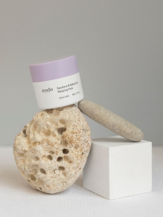 Exfoliating stone and jar of Ondo Beauty Squalane & Bakuchiol Sleeping Pack on a white surface with a gray background