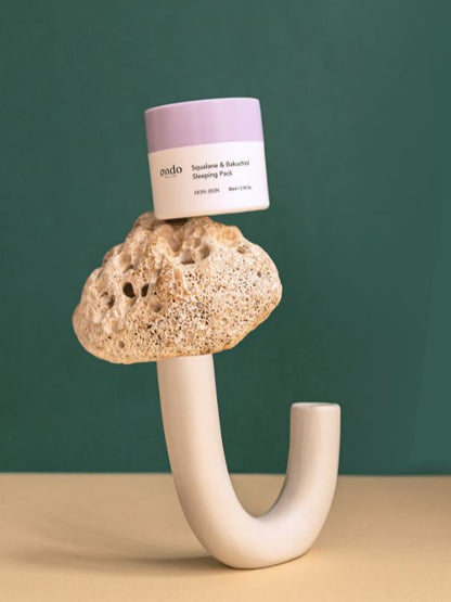 Jar of Ondo Beauty Squalane & Bakuchiol Sleeping Pack on a unique stone holder against a green background