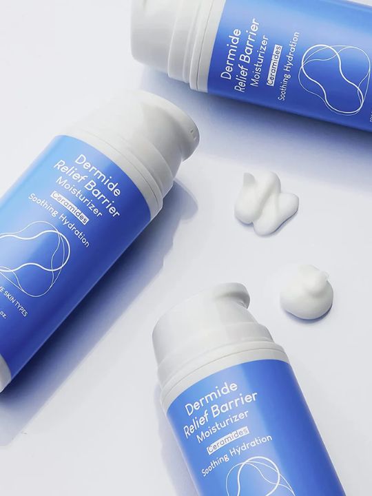 Three bottles of Purito Dermide Relief Barrier Moisturizer lying on their sides with two swatches of white cream, on a white surface