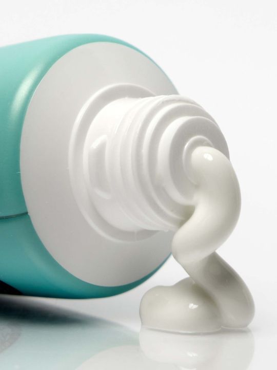 Close-up of Suntique I'm 4 Seasons Hand Suncream with white cream being squeezed out on a white background