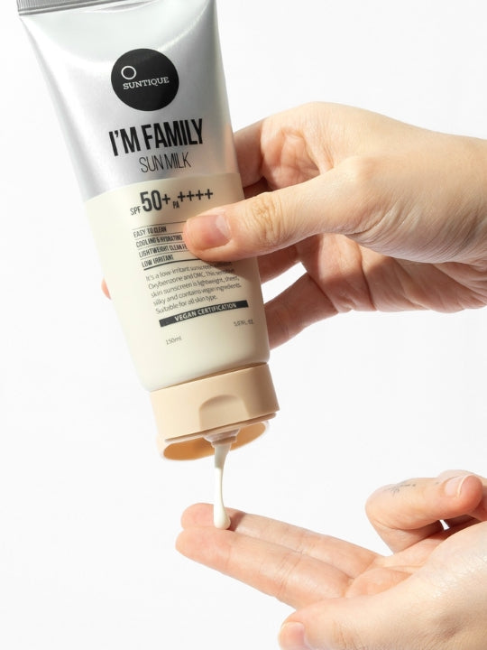 A hand holds a tube of Suntique I'm Family Sun Milk sunscreen, dispensing a thick white cream into another hand against a clean white background.