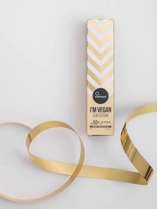 Suntique I'm Vegan Sun Serum packaging with gold ribbon on a light grey background
