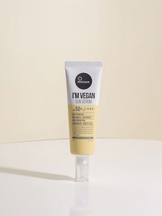 Tube of Suntique I'm Vegan Sun Serum on a white surface and pale yellow background
