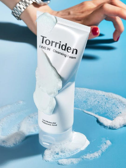 Torriden Dive In Cleansing Foam tube covered in foam and standing on a blue surface with a hand in the background