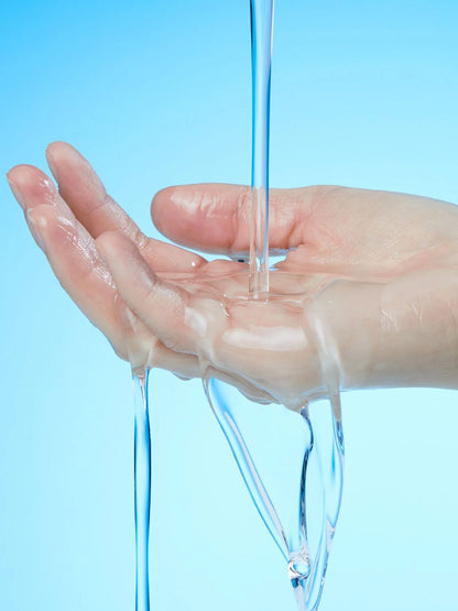 A close-up of a human hand under a stream of clear water against a light blue background.