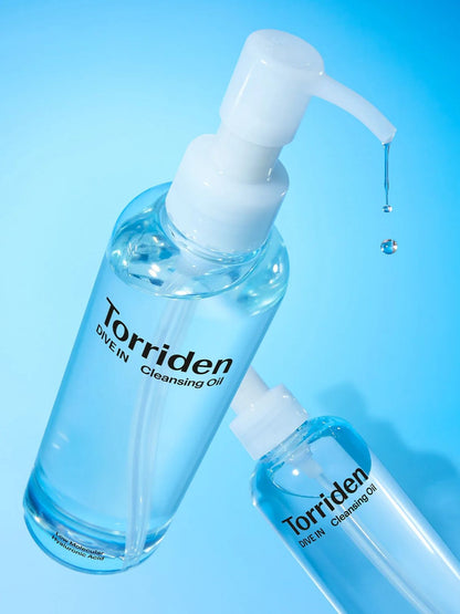 Two clear plastic pump bottles of Torriden Dive-In Cleansing Oil with white pumps, shown on a bright blue gradient background with a single liquid droplet dripping from the larger bottle.