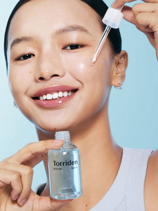 Woman holding a bottle and dropper of Torriden Dive In Low Molecular Hyaluronic Acid Serum on a light blue background