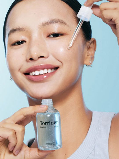 Woman holding a bottle and dropper of Torriden Dive In Low Molecular Hyaluronic Acid Serum on a light blue background