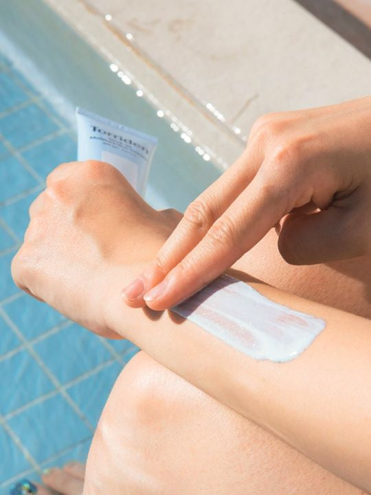 Person applying a patch of Torriden Dive In Moisture Sun Cream to their arm by a pool