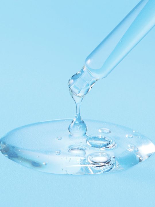 Serum dropper releasing liquid onto a blue surface