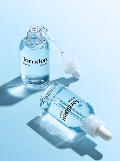 Two bottles of Torriden Dive In Low Molecular Hyaluronic Acid Serum, one open with dropper out and one closed and lying on its side, on a light blue background.