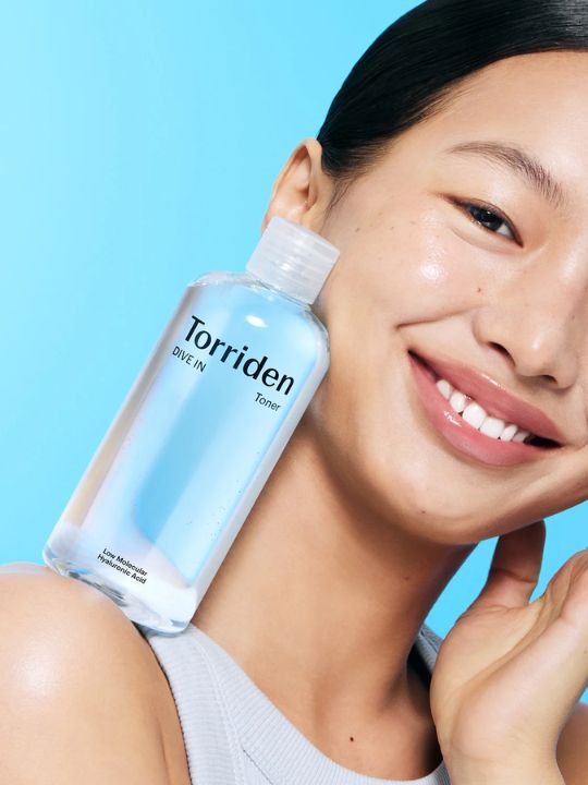 Woman balancing a bottle of Torriden Dive In Toner on her shoulder against a blue background