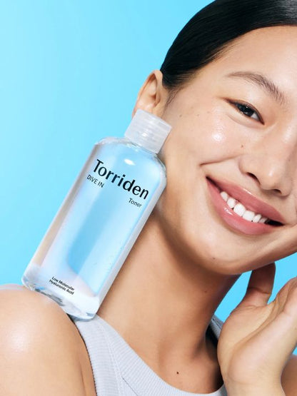 Woman balancing a bottle of Torriden Dive In Toner on her shoulder against a blue background