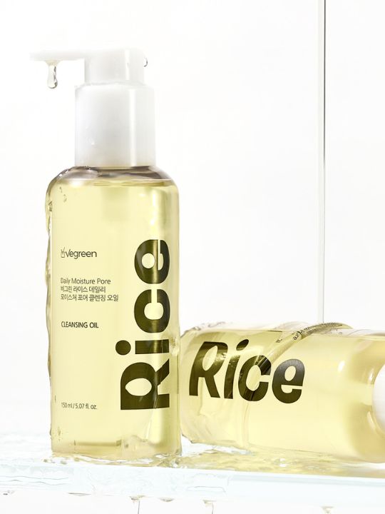 Two pump bottles of Vegreen Rice Daily Moisture Pore Cleansing Oil with liquid running down on a white background