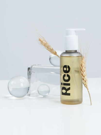 Pump bottle of Vegreen Rice Daily Moisture Pore Cleansing Oil standing next to transparent props and stalks of wheat, against a light background